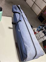 Blue rolling carry case storing hammock and canopy, showing handles and zipper for closure.