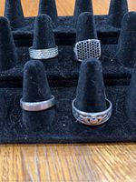 Four men's rings displayed on black ring holder stand showing assorted styles and sizes.