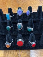 Photo showing nine sterling silver rings with assorted stones on a black ring holder, arranged in three rows.