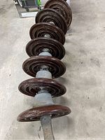 Full view of seven linked ceramic insulators aligned horizontally on a concrete floor showing brown glazed discs and central metal rod joined through the center.