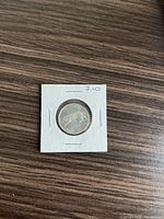 Photo showing a 1967 Canadian silver quarter coin housed in a white cardboard coin flip holder with a price marking of 7.00.