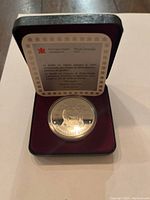 Silver proof dollar coin in a black display case with maroon velvet lining, showing certificate inside lid.