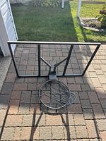 Photo showing basketball net attached to metal rim and rectangular metal-framed backboard with broken glass in center.
