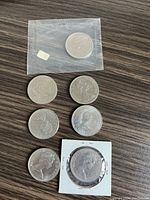 Seven Canadian dollar coins placed on a wooden surface, one coin in original mint packaging, one in coin cardboard holder, five are loose.
