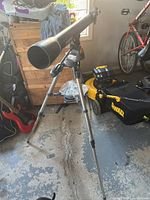 Full view of the Celestron Astronaster 70 telescope mounted on adjustable tripod in indoor space.