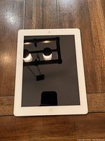 Front view of Apple iPad showing white bezel and black screen with reflection of ceiling lights and camera.