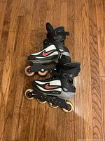 Side view of pair of Nike inline rollerblades, black and white with red swoosh logo, size 8, resting on wooden floor