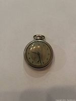 Front view of pocket watch showing dial, Arabic numerals, smaller second dial, and winding crown at the top.