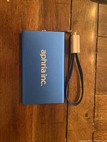 Front view of blue Aphria Inc. power bank with attached cable strap on a wooden surface