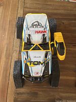 Top-down view of LiteHawk Big Tom 4x4 remote control truck and yellow controller on wooden floor showing body graphics and tracks.