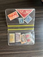 Open plastic sleeve showing eight vintage stamps including two large triangular red stamps and several rectangular ones in various colors.