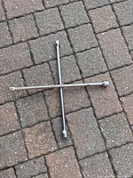 Two cross-shaped tire iron wrenches placed on a stone brick surface, showing front and top views.