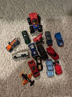 Top view of 13 assorted vintage and newer toy cars and trucks with a small toy plane on a carpeted surface.