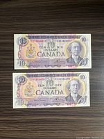 Front view of two vintage Canadian $10 bills placed side by side on a dark wooden surface showing design details and serial numbers
