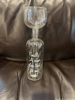 Photo of a clear glass wine glass with white text printed on the side reading 'Finally! A wine glass that fits my needs!' The glass has an unusual design with the stem portion inside the bowl.