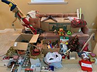Photo showing entire assortment of Christmas decorations on a sofa and floor including large reindeer figure, boxes, baskets, wrapping paper rolls, wreath, pinecones, and assorted smaller decorations
