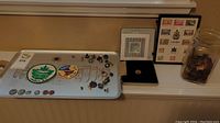 Collector's tray with assorted pins, coins, and stamp sheets displayed alongside jar of coins