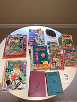 Photo of table with assorted comic books featuring titles such as Marvel Spider-Man, Archie, Looney Tunes, Pink Panther, Riverdale High and Disney comics arranged in stacks.