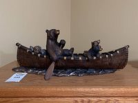 Front view of sculpture showing two bears in a canoe with a paddle and camping gear.