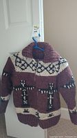 Full view of the brown and cream kids wool jacket with cross designs hanging on a door.