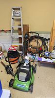 Wide view showing the Craftsman electric lawn mower, shop vacuum, ladders, coiled hose, and other garden tools.