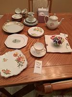 Photo showing an assortment of plates, cups, a floral fabric arrangement and a floral teacup with saucer on a wooden table.