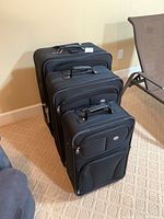 Three black American Tourister luggage pieces arranged by size with handles extended.