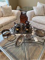 Full view of Marlboro silver plated coffee and tea set with multiple serving trays on glass table between two white armchairs.