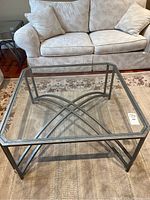 Metal frame octagonal coffee table with glass top in front of a beige sofa on a rug.