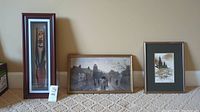 Lot of three framed art pieces against a beige wall showing the carvings and paintings.