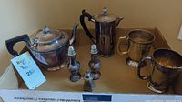 Silver plated coffee pot, teapot, creamer pot, two cups, and salt & pepper shakers arranged in a cardboard box showing the entire set with some tarnish and usage marks