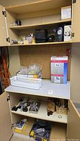 Full shelving unit with tools and hardware organized on multiple shelves including boxes, small tools, and miscellaneous items.