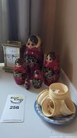Photo showing five Russian nesting dolls, a blue Wedgwood dish with white relief and four napkin rings, and a brass clock