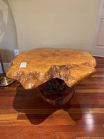 Front view of live edge wood table showing the irregular wood slab top and the tree root base on hardwood flooring.