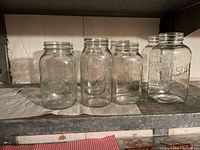 Eight clear glass mason jars of varying size on a shelf, no lids visible.