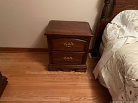 Nightstand positioned next to a bed on hardwood floor, showing overall design and condition.