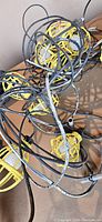 Overhead photo showing tangled black cords with attached yellow protective light cages on a box, some cages broken or cracked.