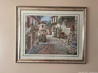 Full view of the framed painting depicting a European village street scene, showing frame and painting details.