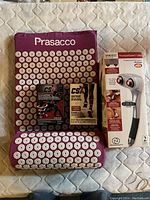 Photo showing purple Prasacco acupuncture mat and pillow with numerous spiked discs, box of CSX compression sports socks, and boxed Homedics percussion massager.