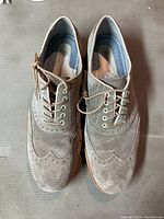 Top down view of the pair of gray sheepskin wingtip dress shoes showing lace-up fronts with metallic eyelets, brogue detailing, and texture of suede material.