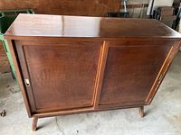 Front view of the vintage wooden dresser with two sliding doors closed, showing wood finish and legs.