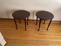 View of both matching side tables placed on wooden floor, showing full height and round tabletops