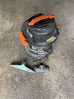 Ridgid shop vacuum cleaner with large flat green nozzle and small black nozzle attachments placed on ground next to unit