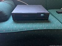 Front view of Sanyo VCR showing digital display, control buttons, and black chassis on a green fabric surface.