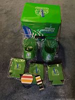 Green metal Steam Whistle cooler with logo, opener, three drink koozies, and two shower caddies arranged on floor