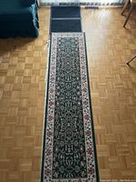 Full view of one forest green area rug runner on wood floor, showing overall design and condition.