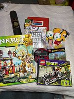 Lot showing LEGO Ninjago, LEGO Teenage Mutant Ninja Turtles, Monkey Kid set, plush toys, vintage Battleship, puzzle, dartboard, and McDonalds toy
