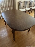 Top view of a traditional oval wooden dining table with a visible wood grain finish, surrounded by high-back upholstered chairs.