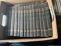 Photo showing all 14 volumes of the 1935 Compton's Encyclopedia set in a cardboard box, spines visible with alphabetical volume labels and Compton Company branding.
