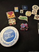Top view of front of assorted quilting event pins with colorful quilt block designs and location names